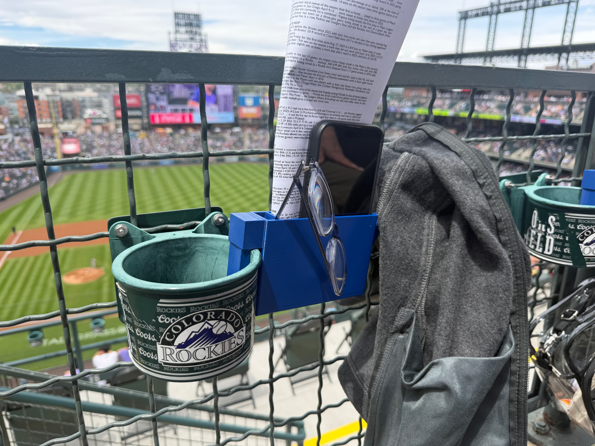 SNAC-KLIP installed on a stadium rail holding a phone, glasses and game notes
